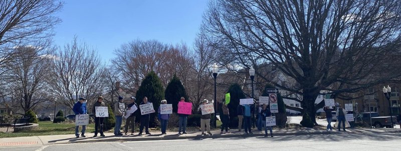 photo of protestors with signs out on a town square on a sunny day